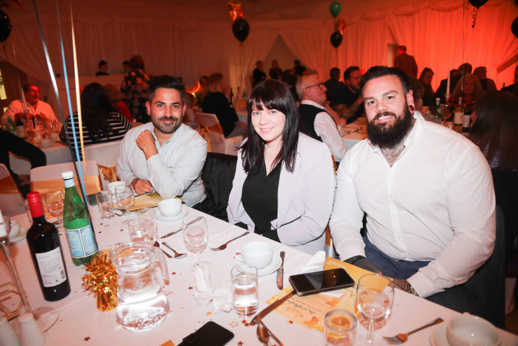 Three people sat at a table smiling for a photograph at the Star Awards 2022